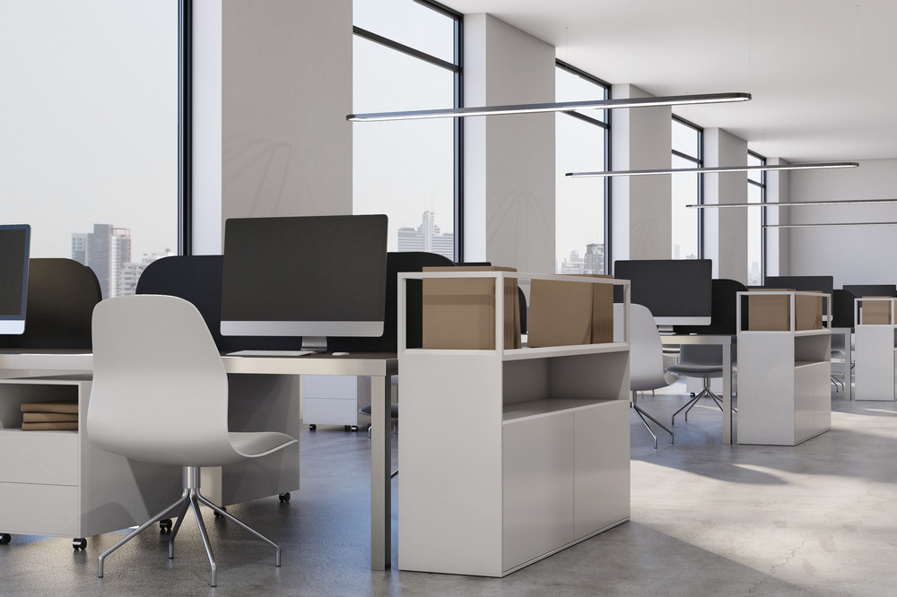 Spacious, modern office with rows of workstations, ergonomic chairs, large windows, and natural lighting, creating an open and organized workspace.